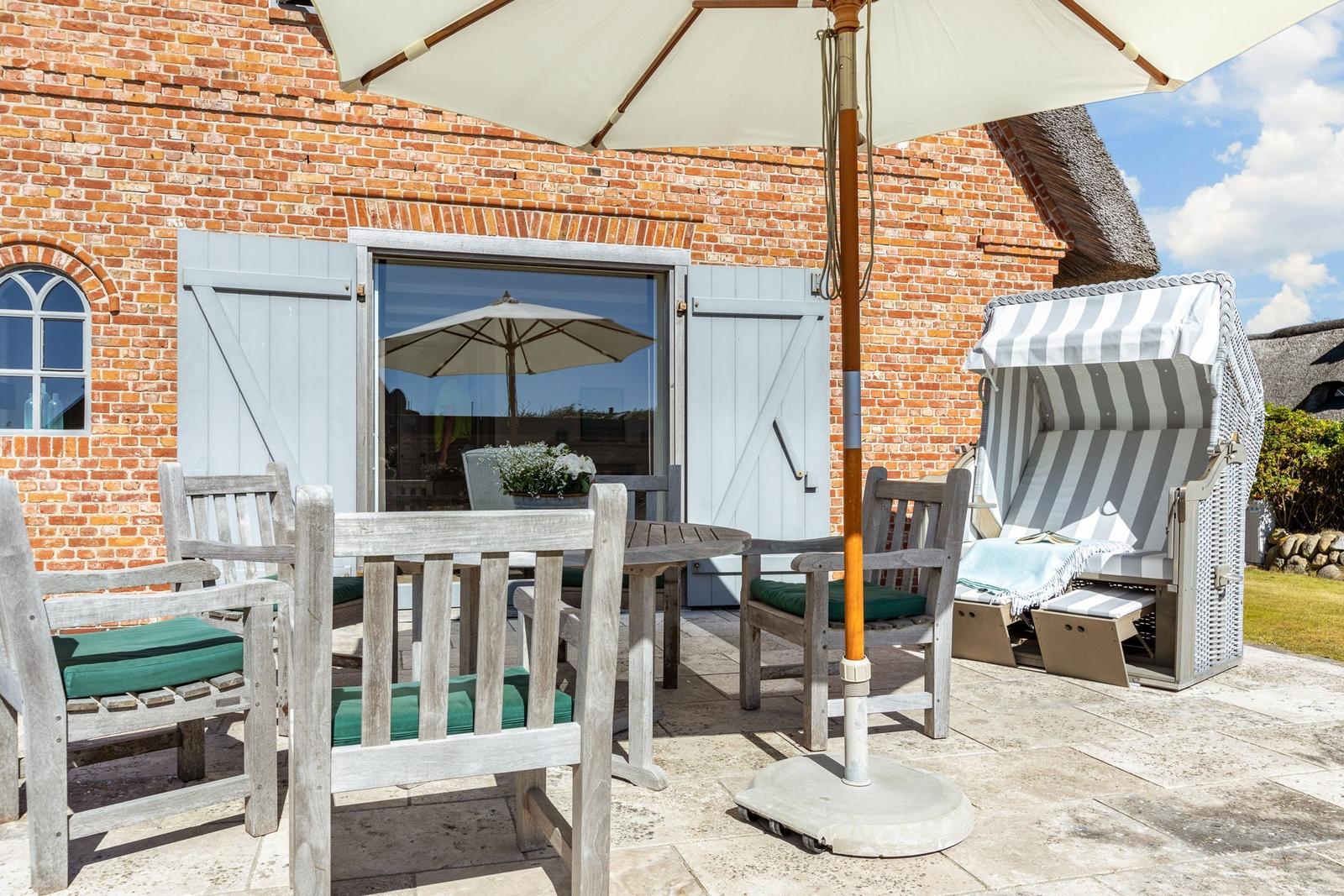 Terrasse mit Tisch, Stühlen, Sonnenschirm und Strandkorb vor Backsteinhaus