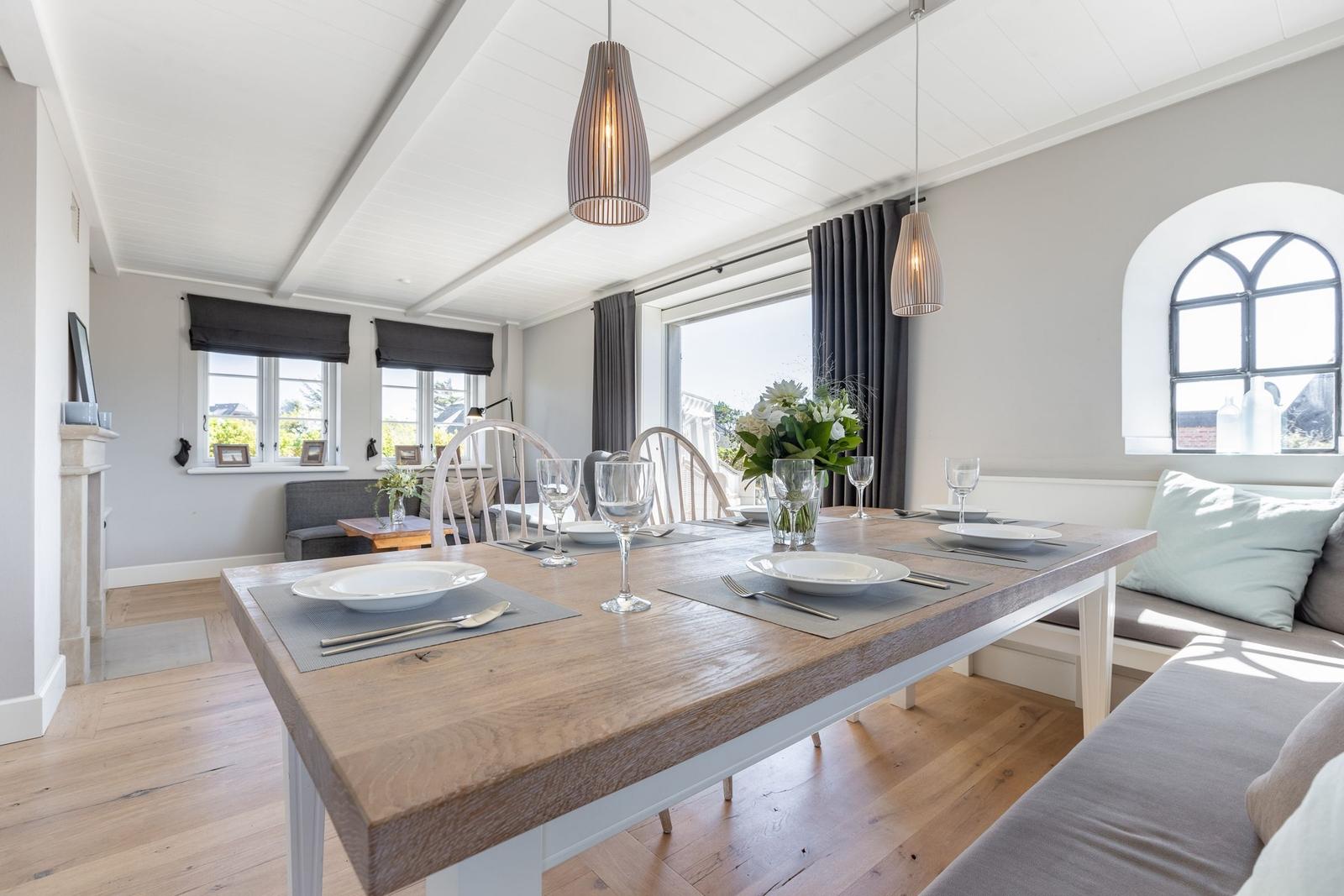 Essbereich mit Holztisch, Stühlen und Fenstern. Helle Wände und Holzboden.