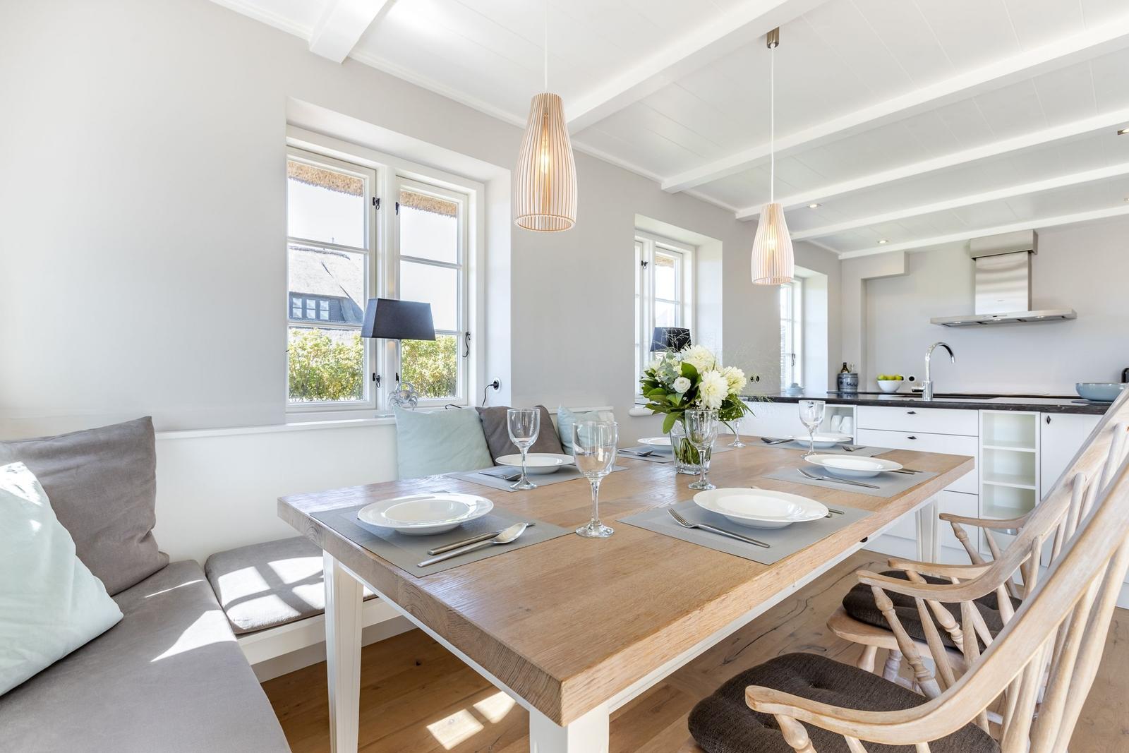 Essbereich mit Holztisch, Stühlen und Fensterblick. Küche im Hintergrund.