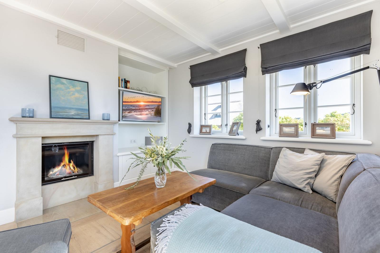 Wohnzimmer mit Kamin, Sofa und Fenstern mit Blick nach draußen.