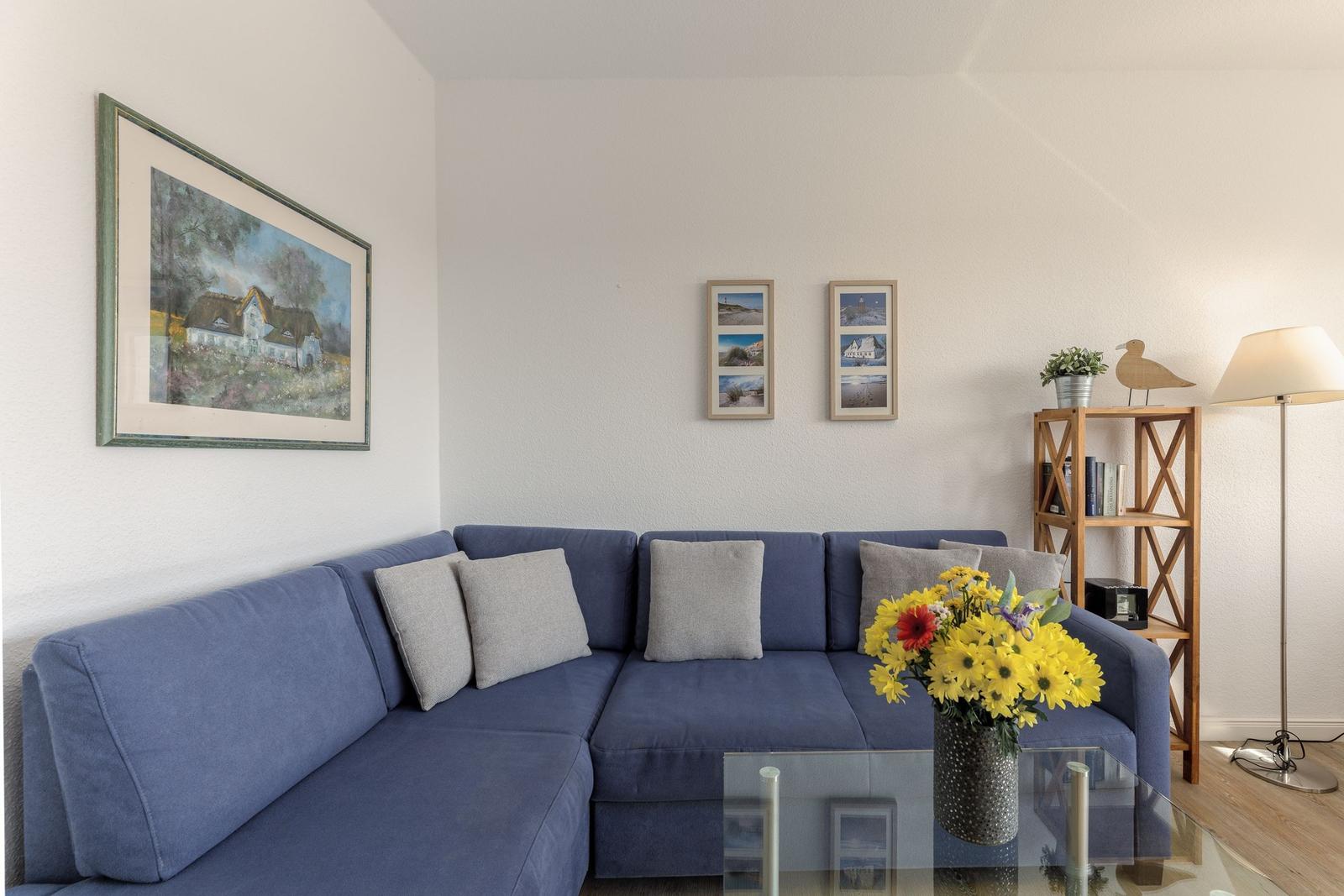 Ein Wohnzimmer mit blauem Sofa, Glas-Tisch und Wandbildern.