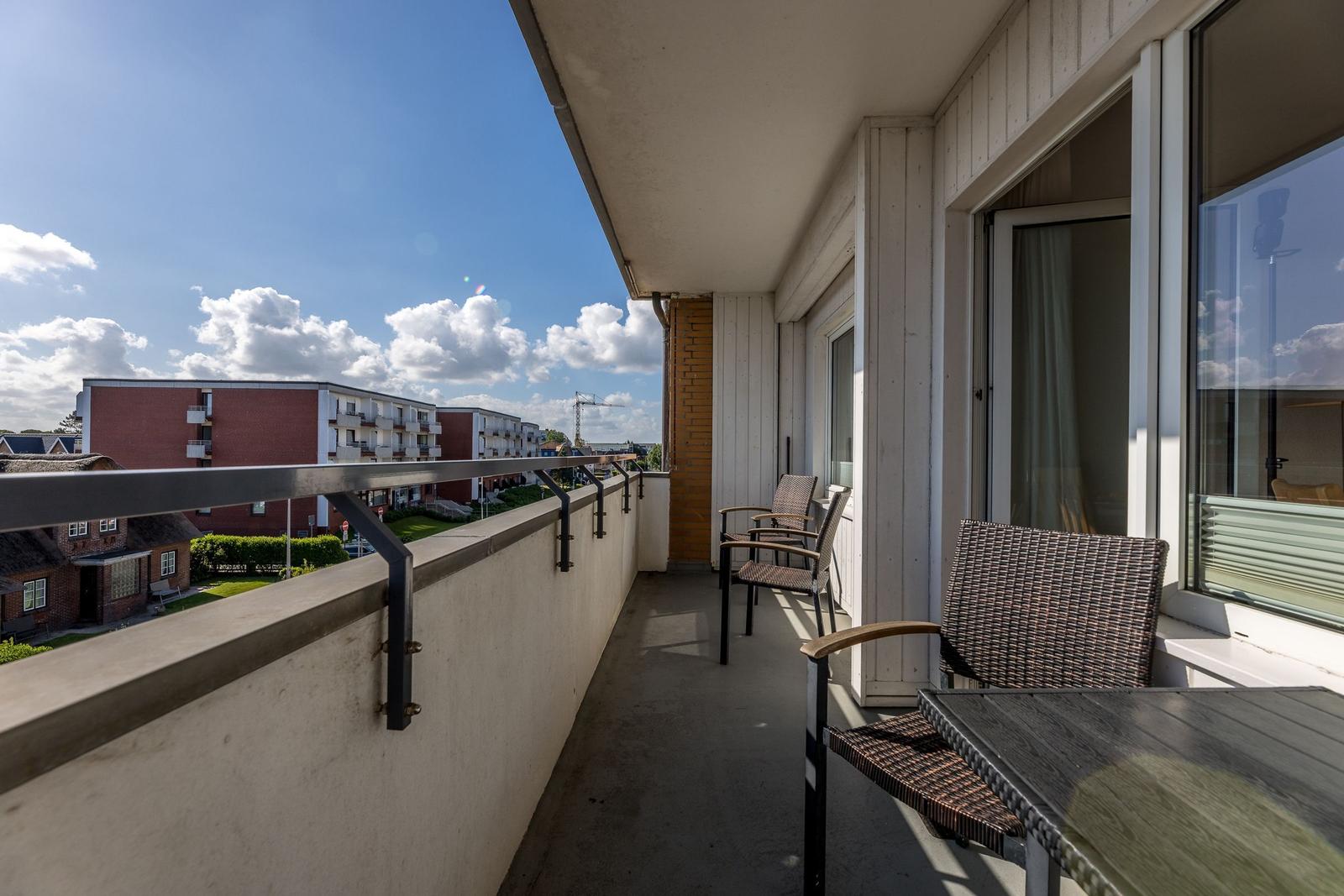 Terrasse mit Sitzgelegenheit und Blick auf Wohnhäuser und Himmel.
