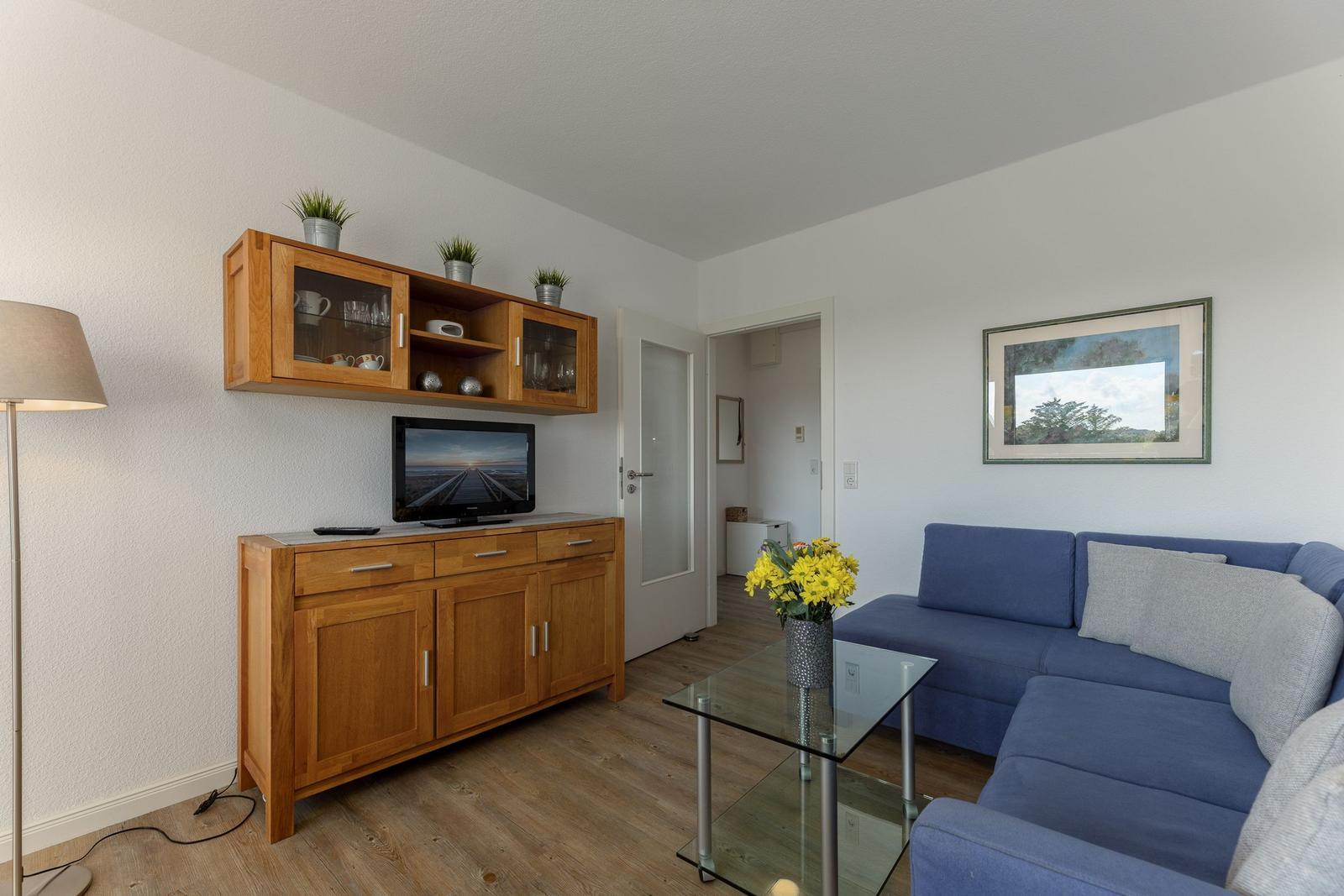 Wohnzimmer mit blauem Sofa, Glas-Tisch und Holzmöbeln.