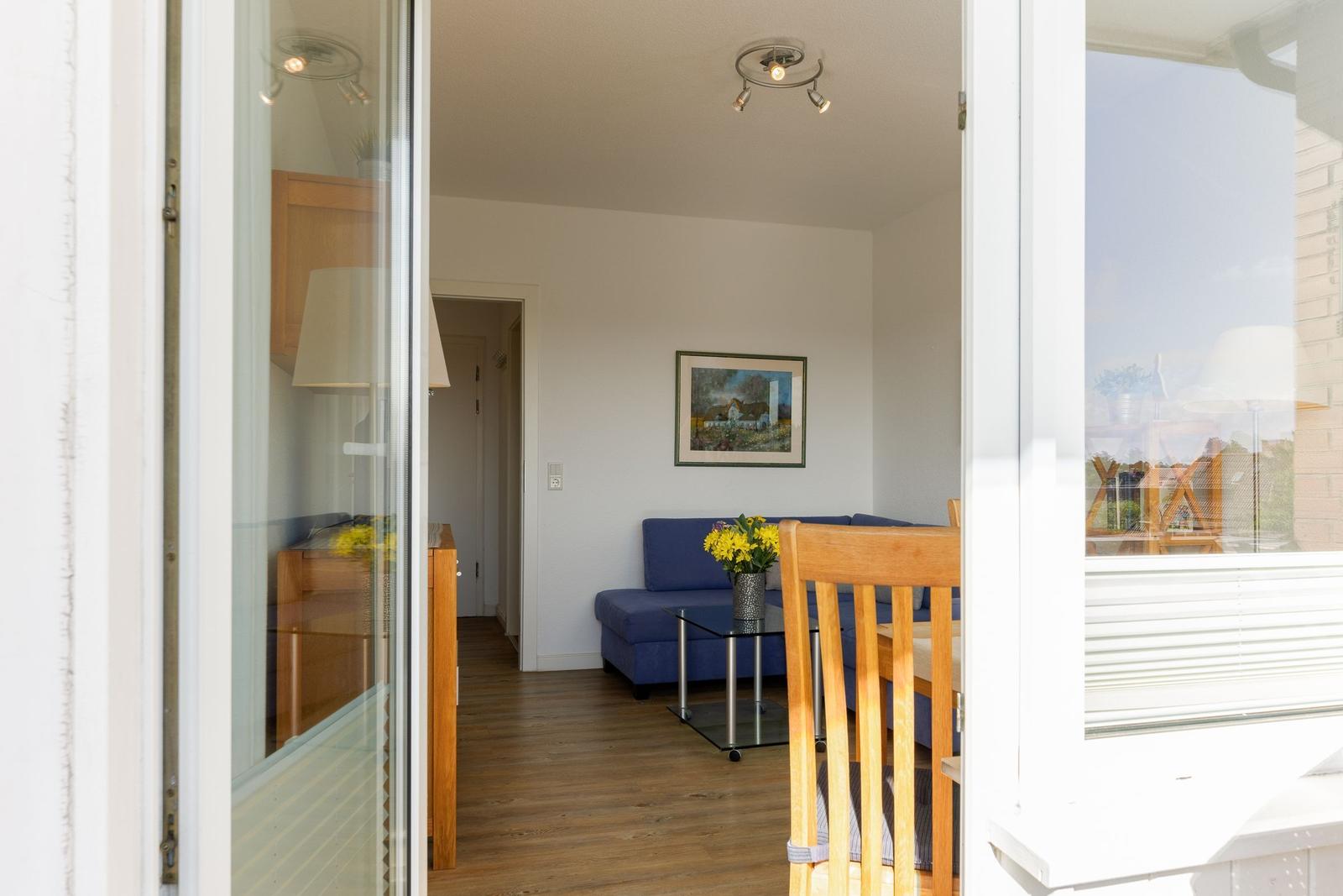 Wohnzimmer mit blauem Sofa, Glasplatte und Holzboden. Fenster zeigt Balkon.