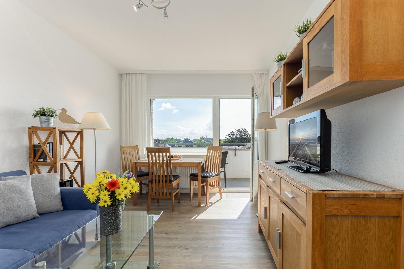 Wohn- und Essbereich mit Balkon, Holzmöbeln und Fernseher.
