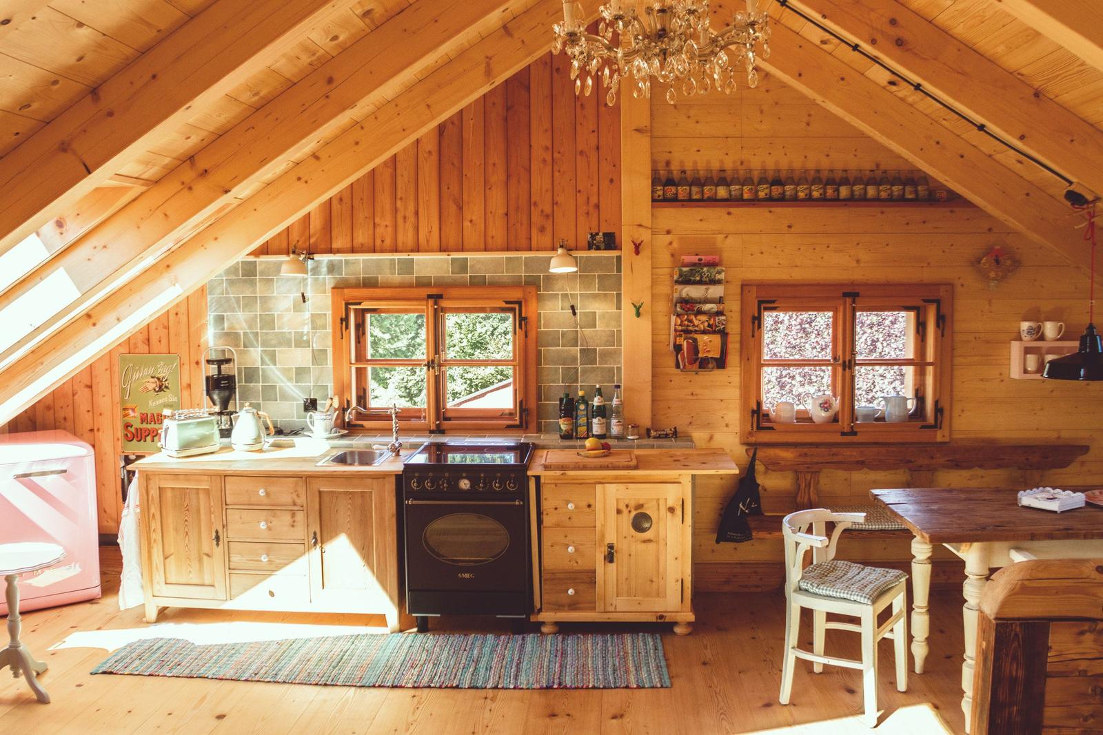 Küche mit Holzmöbeln, Fenstern und Deckenbalken. Ein rosa Kühlschrank und eine Arbeitsplatte sind sichtbar.
