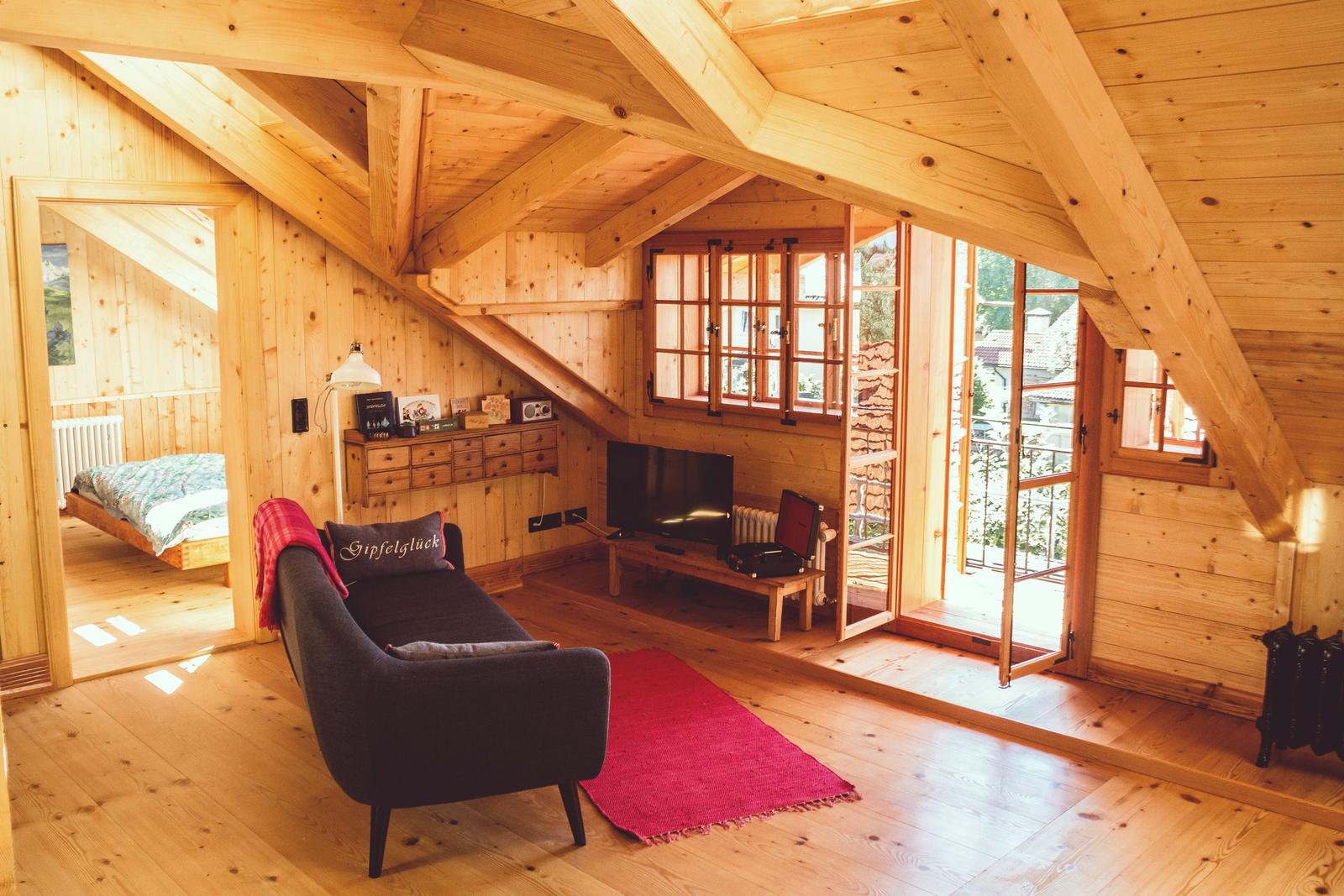 Wohnraum mit Sofa, Fernseher und Blick auf Balkon. Im Hintergrund Schlafzimmer mit Bett.