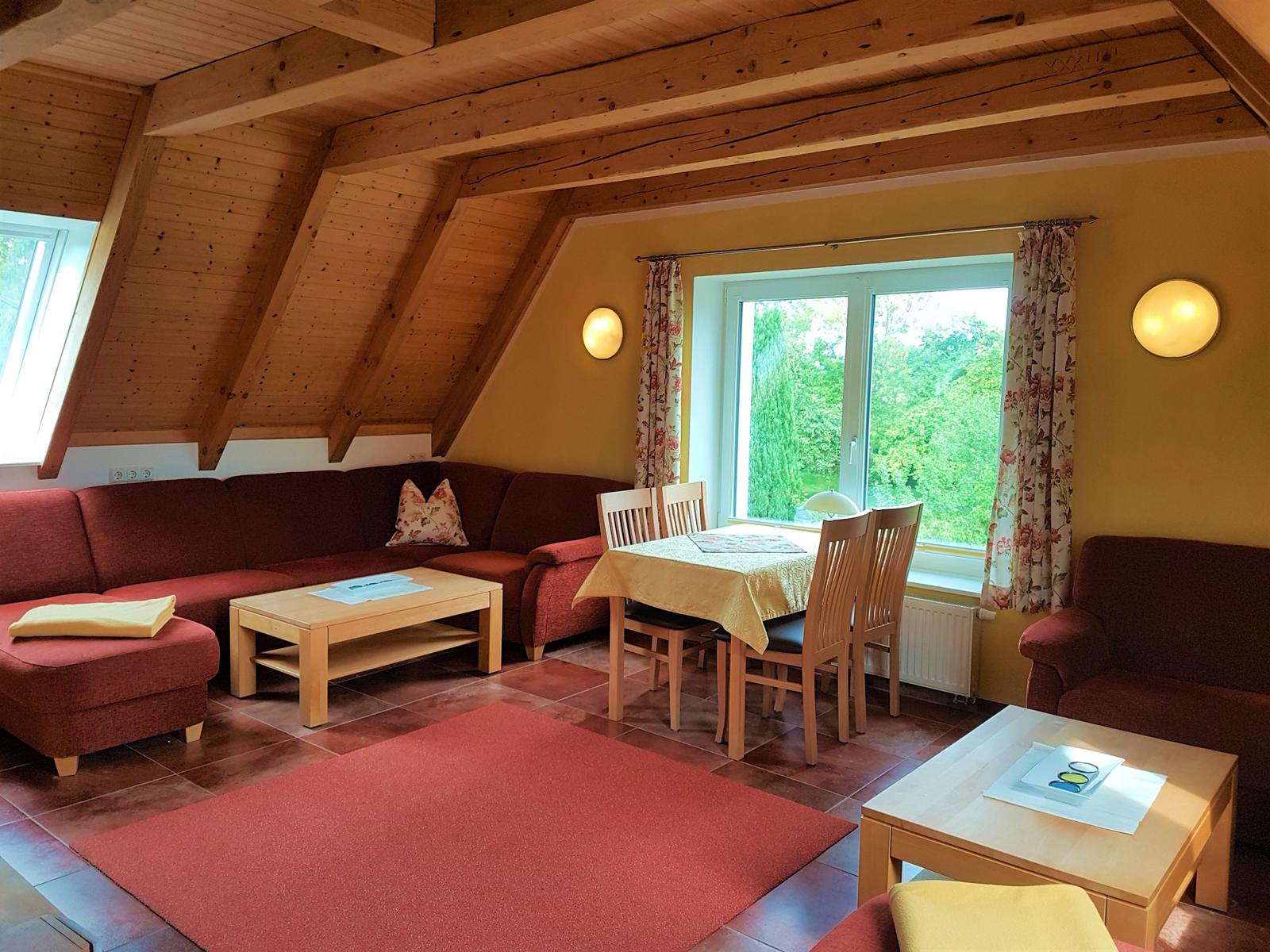 Wohn- und Essbereich mit Holzdecke, rotem Sofa und Tisch mit Stühlen.