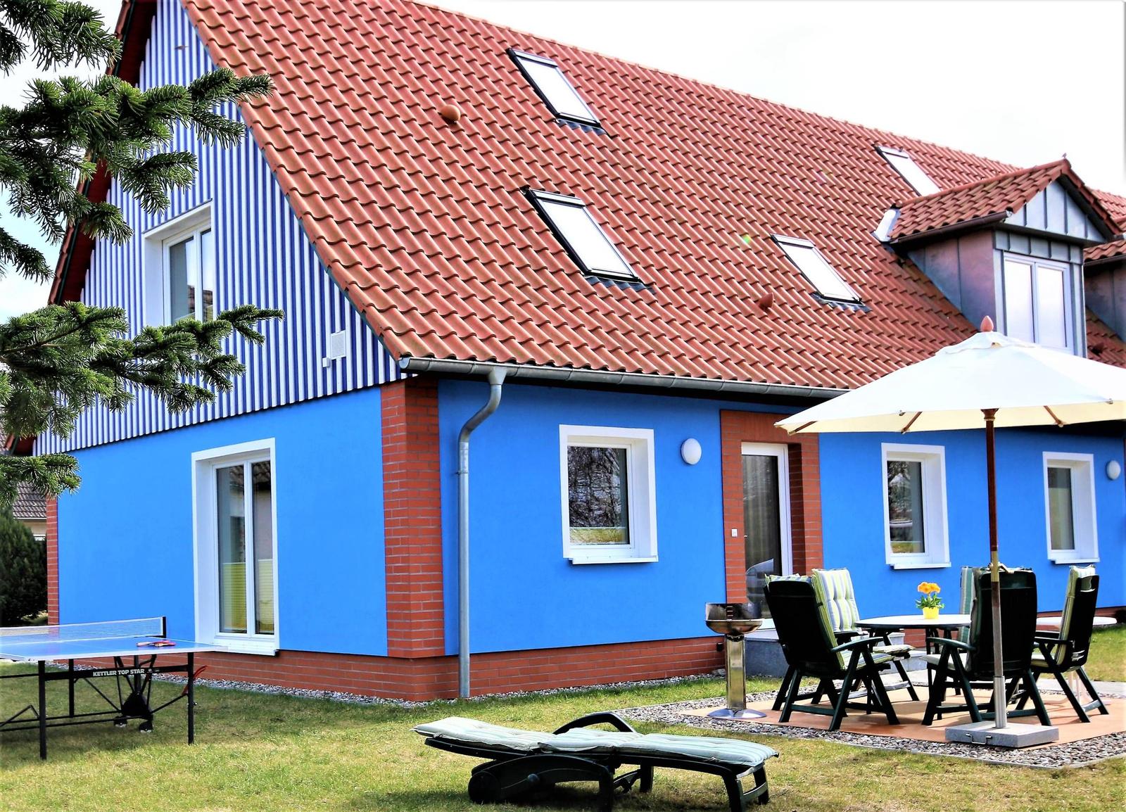 Blau gestrichenes Haus mit rotem Dach und Gartenmöbeln.