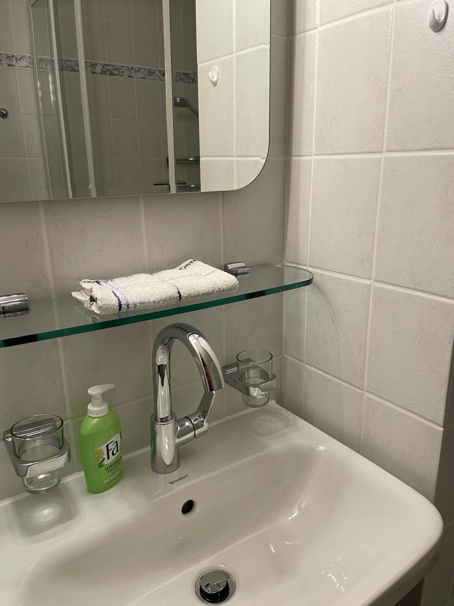 Waschbecken mit Spiegel und Handtuch auf Glasregal.