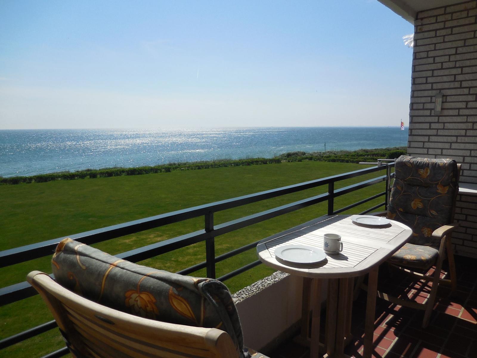 Terrasse mit Tisch und Stühlen, Blick auf grünes Feld und Meer.