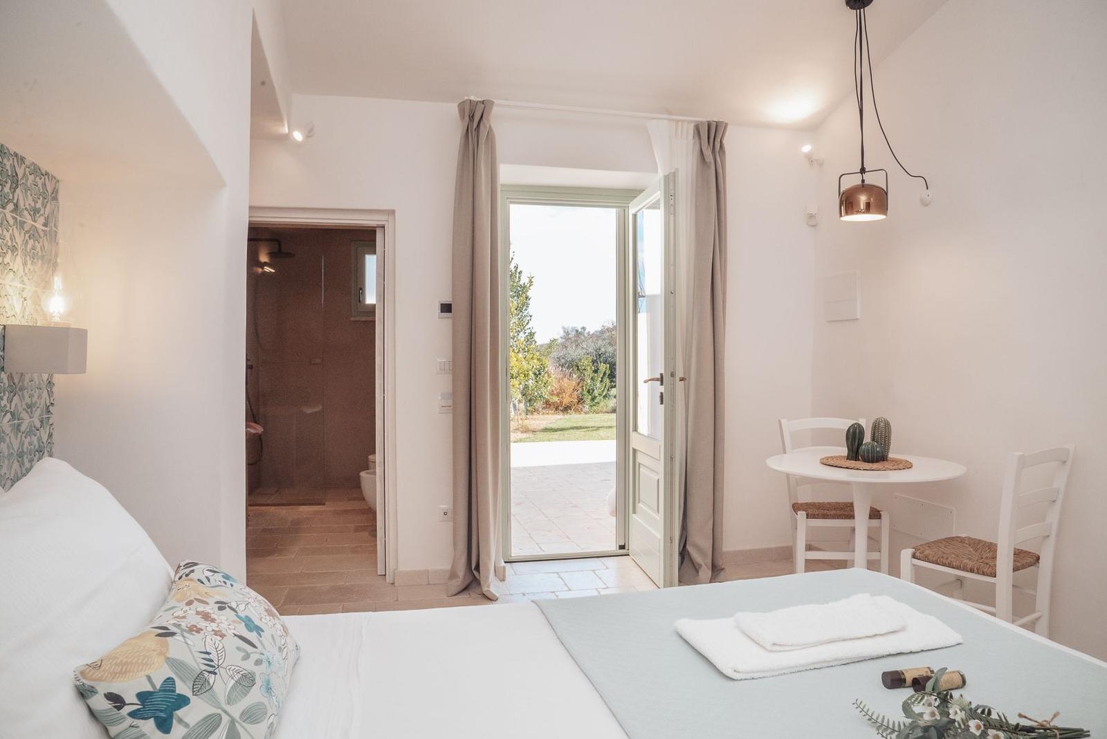 Bedroom with view to balcony, small table, and bathroom in background.