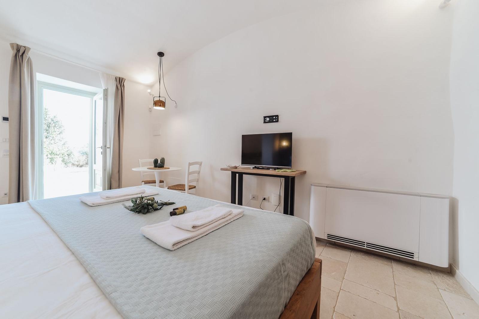 Bedroom with bed, TV, and table with chairs. Window with view outside.