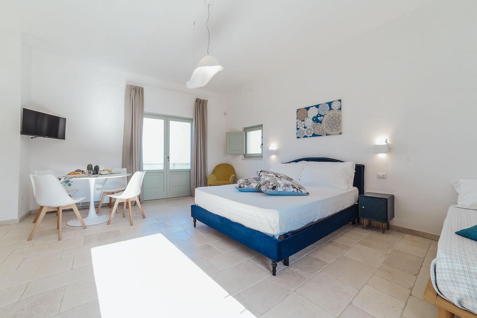 Schlafzimmer mit Bett, Esstisch und Fenster. Wandbild und Nachttisch sind sichtbar.