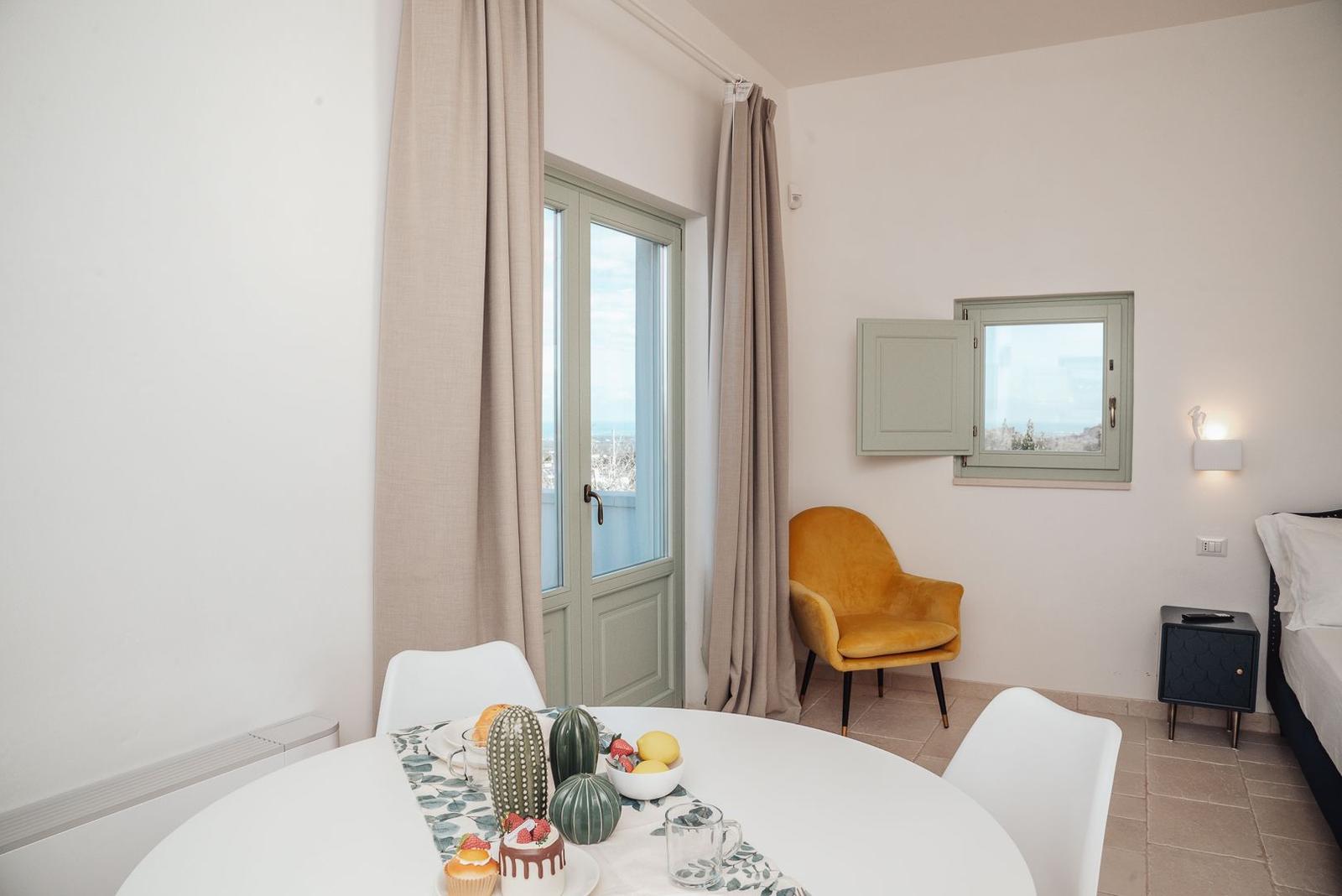 Rundtisch mit Früchten, gelber Sessel, Fenster und Balkontür.