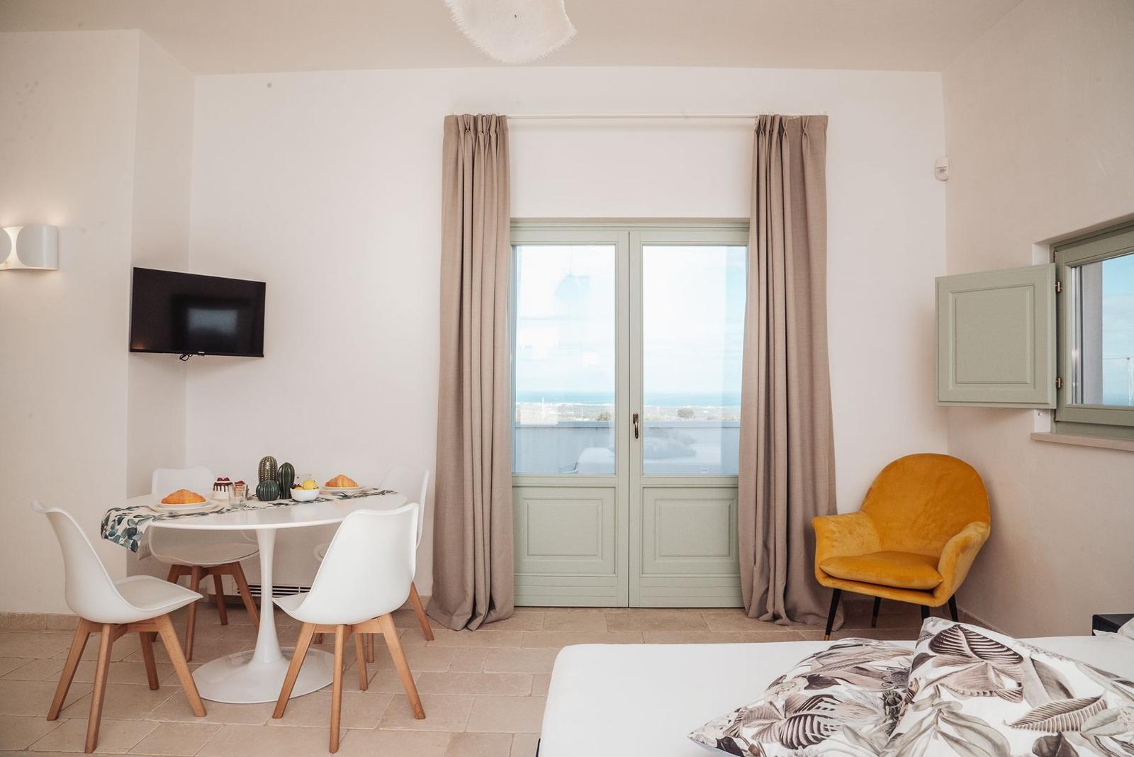 Schlafzimmer mit Essbereich, Bett, gelber Sessel und Fenster mit Meerblick.