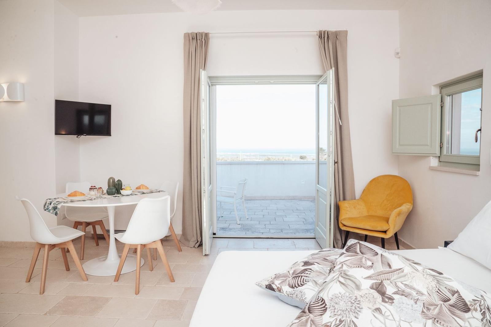 Schlafzimmer mit Blick auf Balkon und Meeresblick. Gelber Sessel, Essbereich und TV.