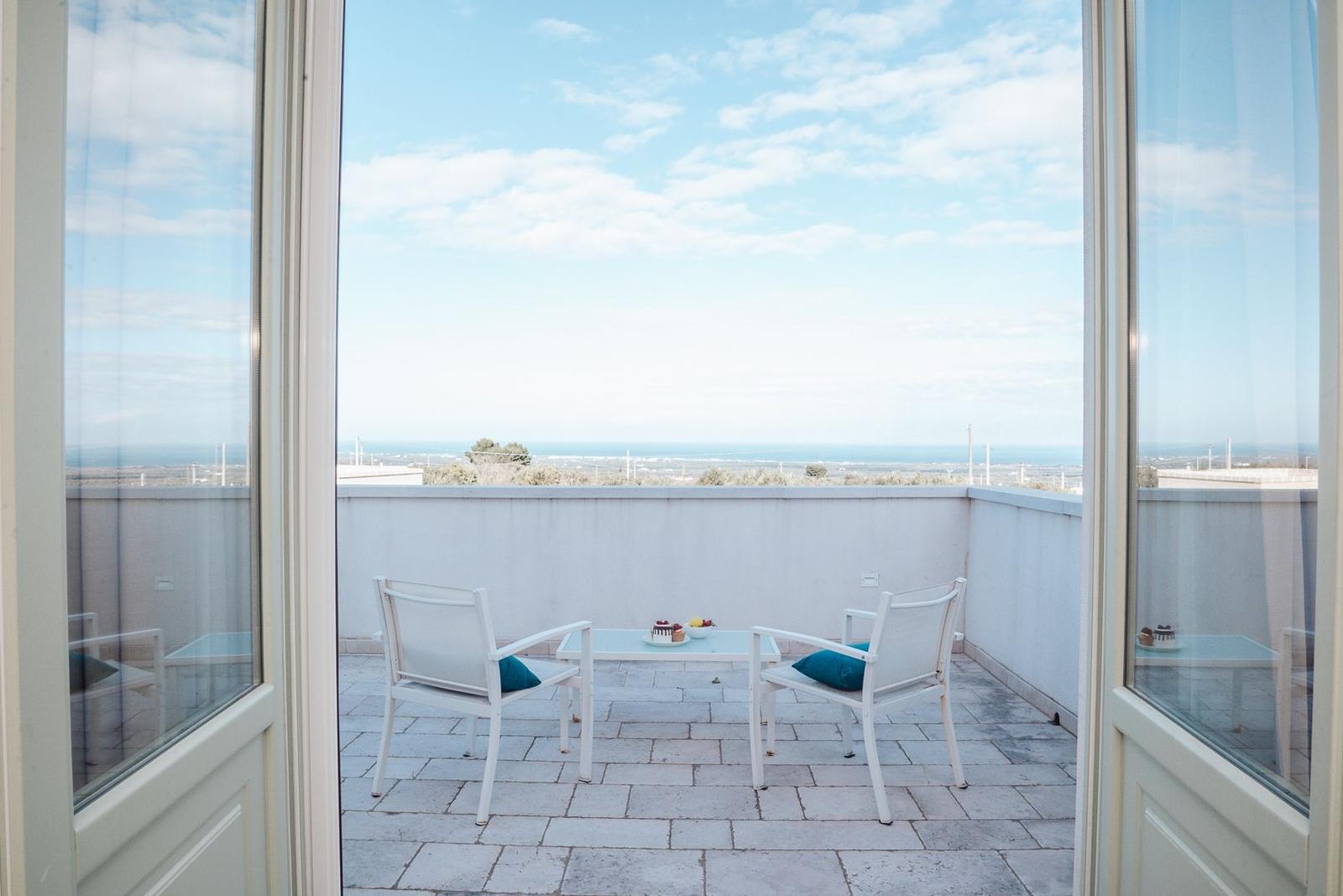 Terrasse mit zwei Stühlen und Tisch. Blick auf Meer und Landschaft.