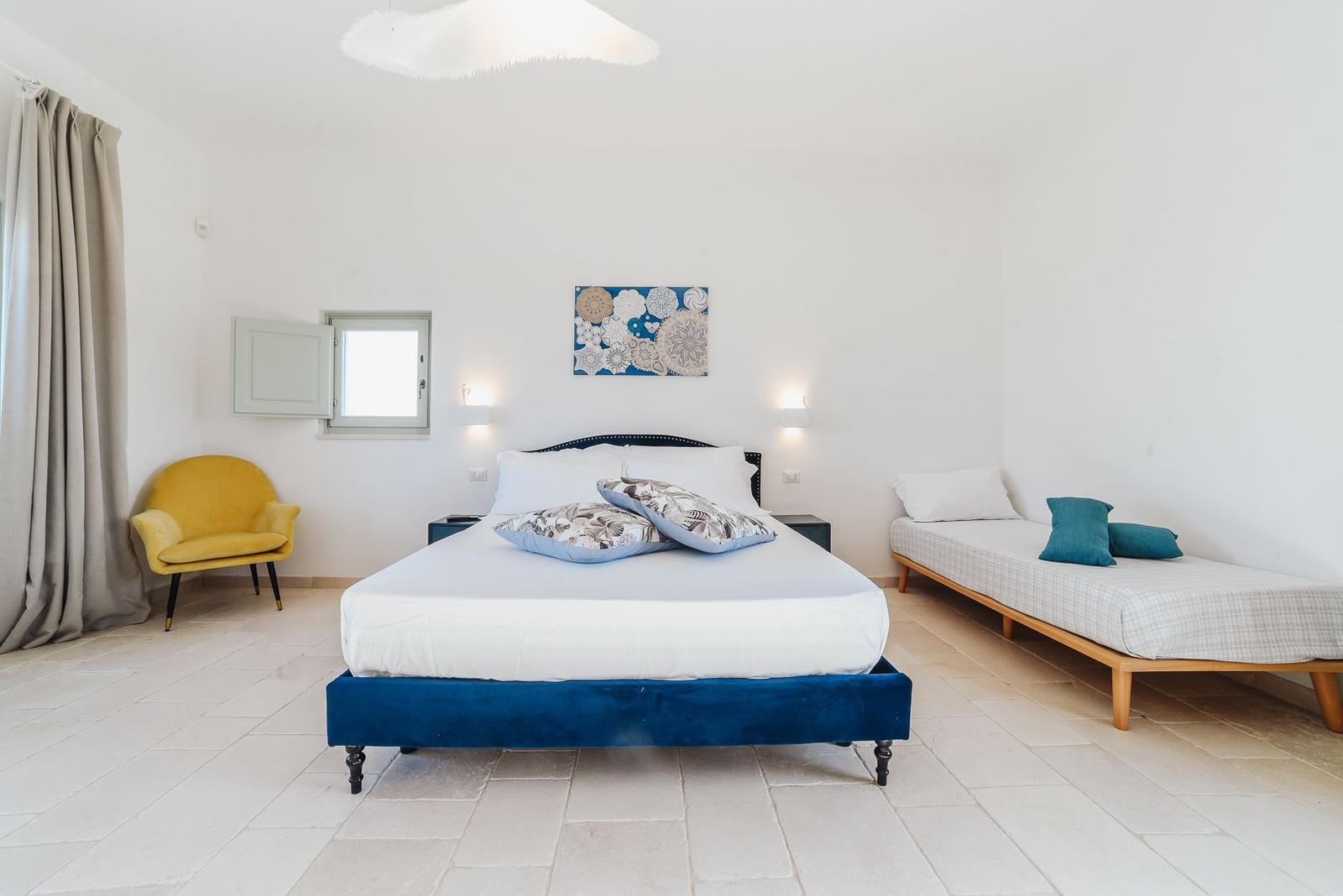 Schlafzimmer mit Bett, Sitzbank und gelber Sessel.