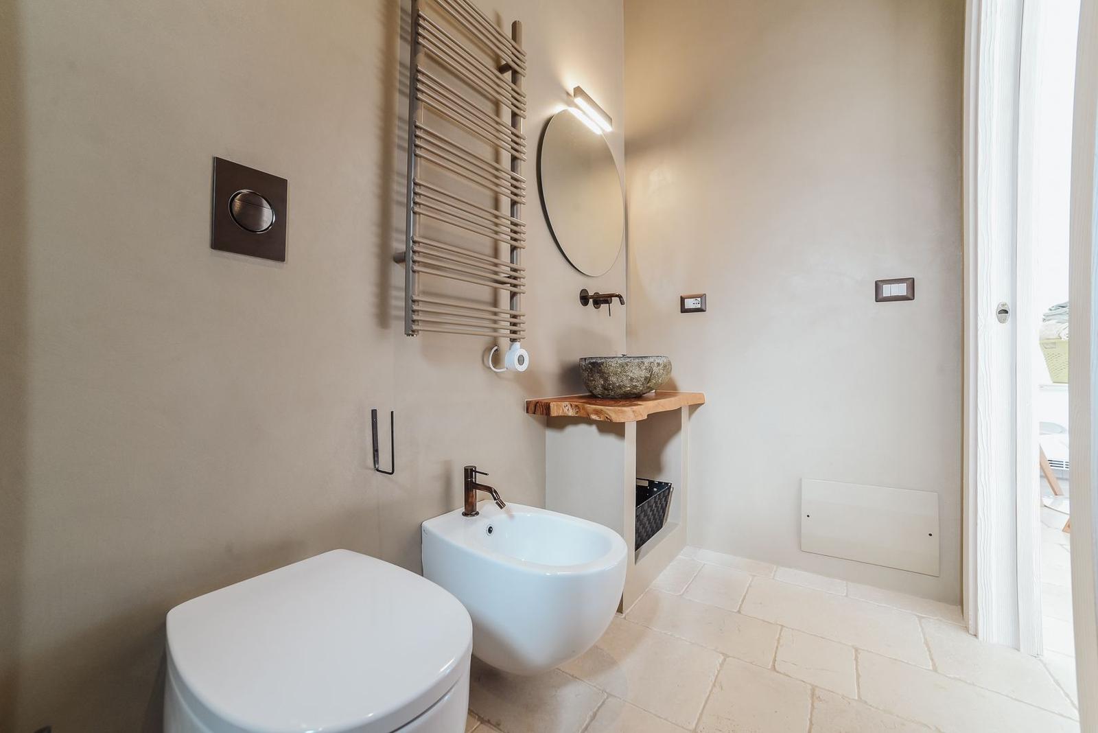 Badezimmer mit Toilette, Bidet und Steinwaschbecken auf Holzunterschrank