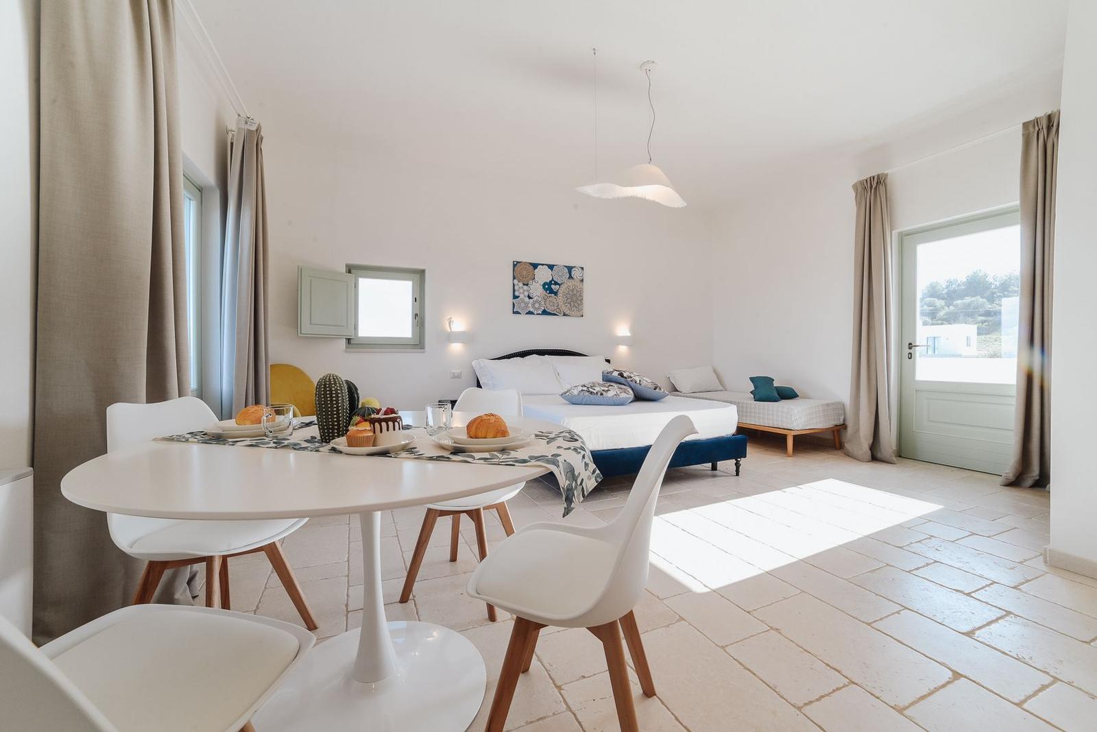 Ein Raum mit Schlafplatz, Esstisch und Fenster. Ein modernes Interieur mit weißen Wänden.