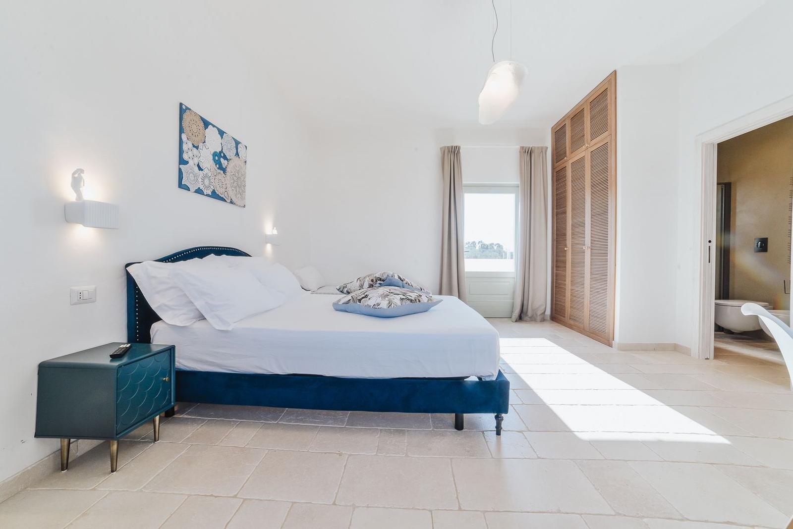 Schlafzimmer mit Bett, Nachttisch und Kleiderschrank. Blick in das Badezimmer.