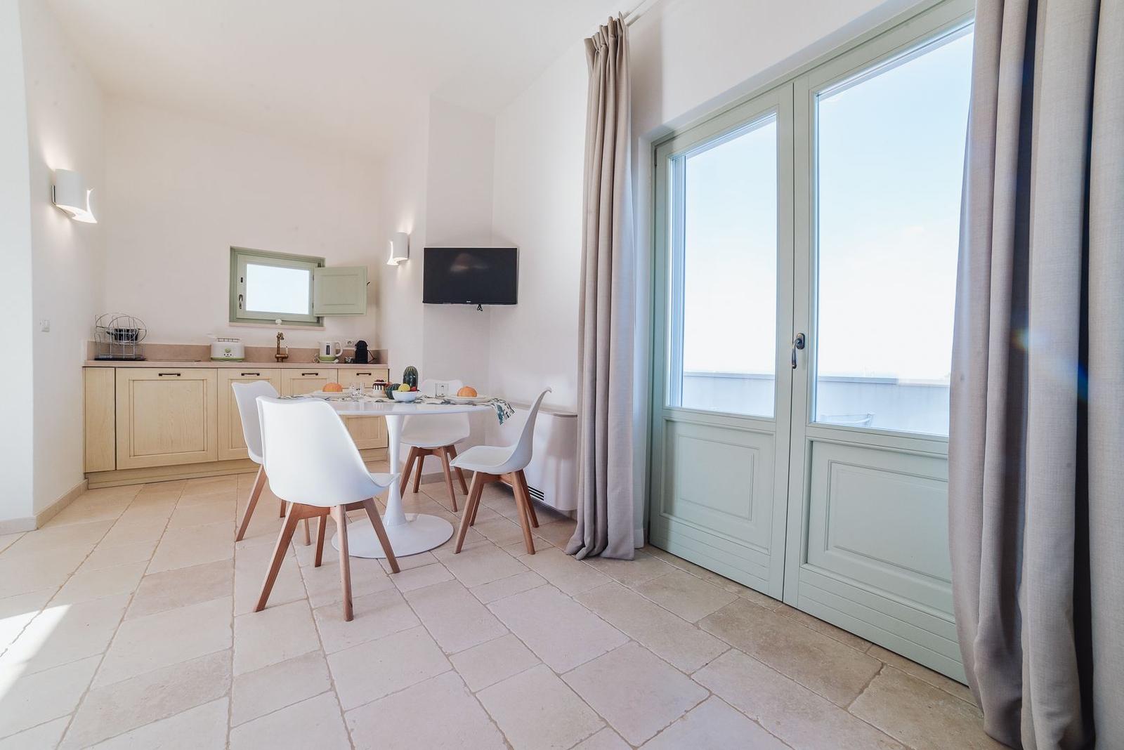 Essbereich mit Küchenzeile und Balkontür. Weiße Stühle um runden Tisch.