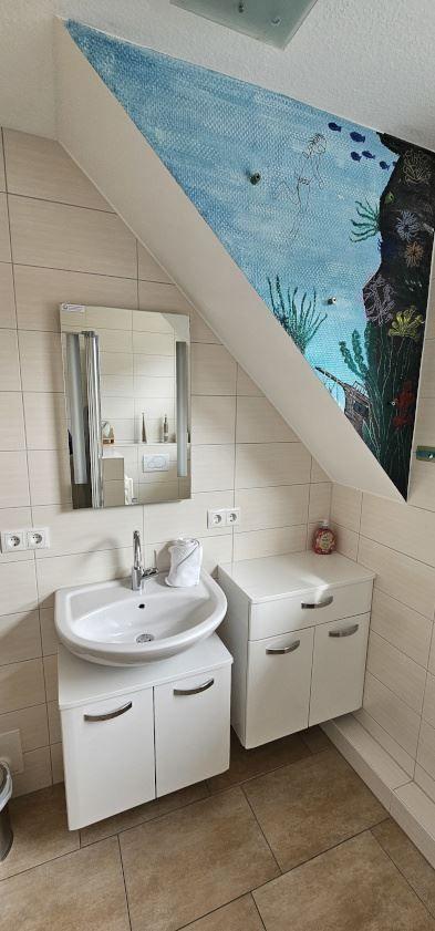 Badezimmer mit Waschbecken, Spiegel und Wandbild unter Dachschräge