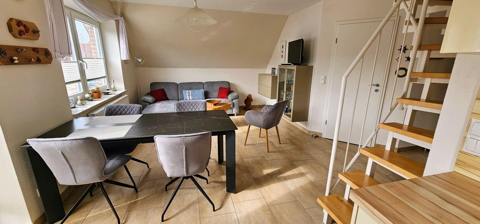 Wohn- und Essbereich mit Sofa, Tisch und Stühlen. Holztreppe führt nach oben.