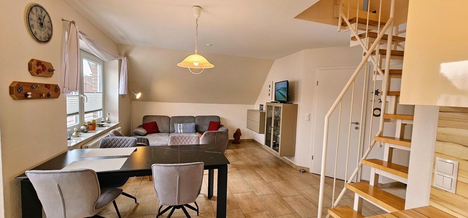 Wohn- und Essbereich mit Sofa, Tisch und Stühlen. Holztreppe führt nach oben.
