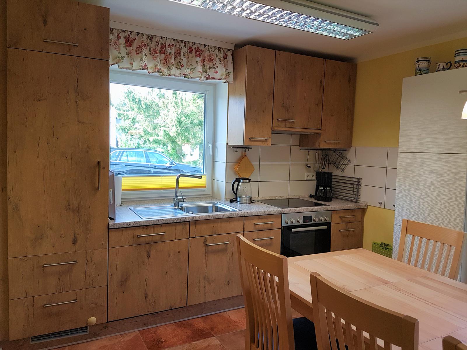 Küche mit Holzschränken, Tisch und Stühlen, Fenster mit Blick nach draußen.