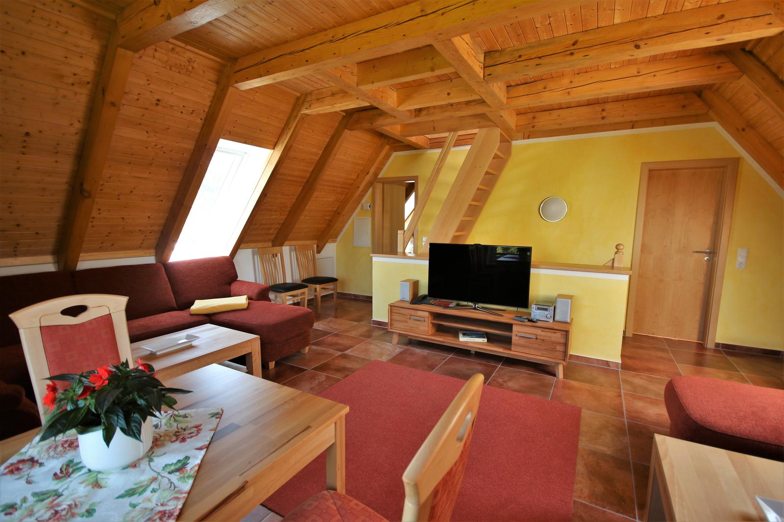 Wohnraum mit Holzdecke, Sofa, Fernseher und Essbereich.