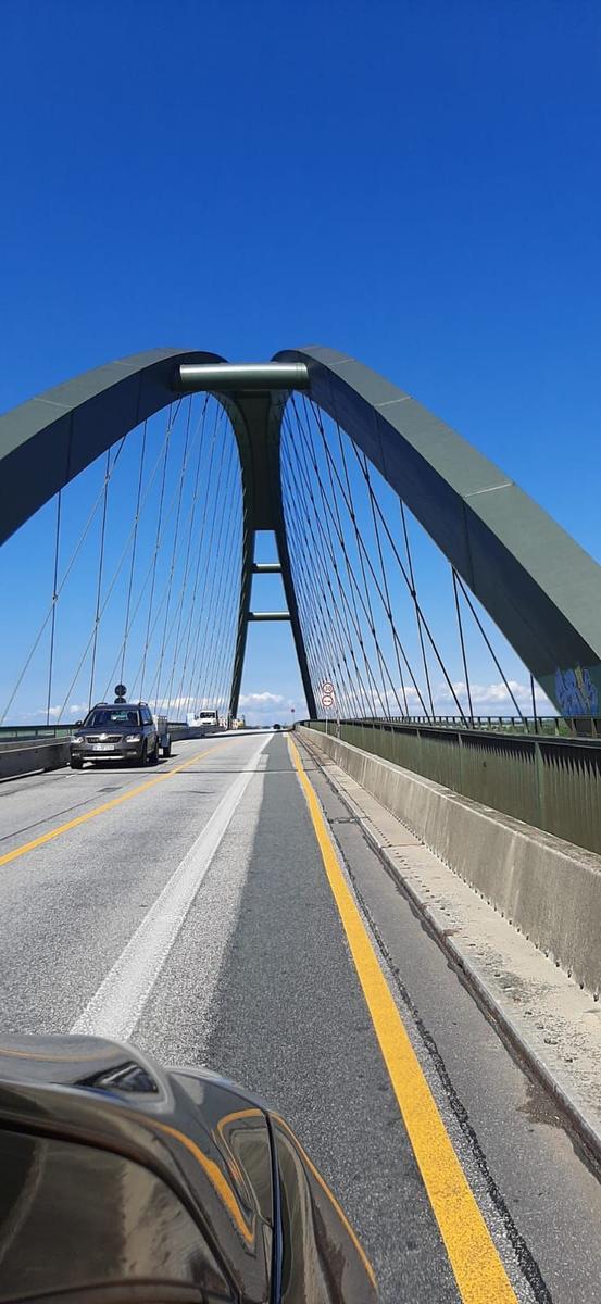 Fahrzeug auf Brücke mit markanter Bogenstruktur und klarem Himmel.