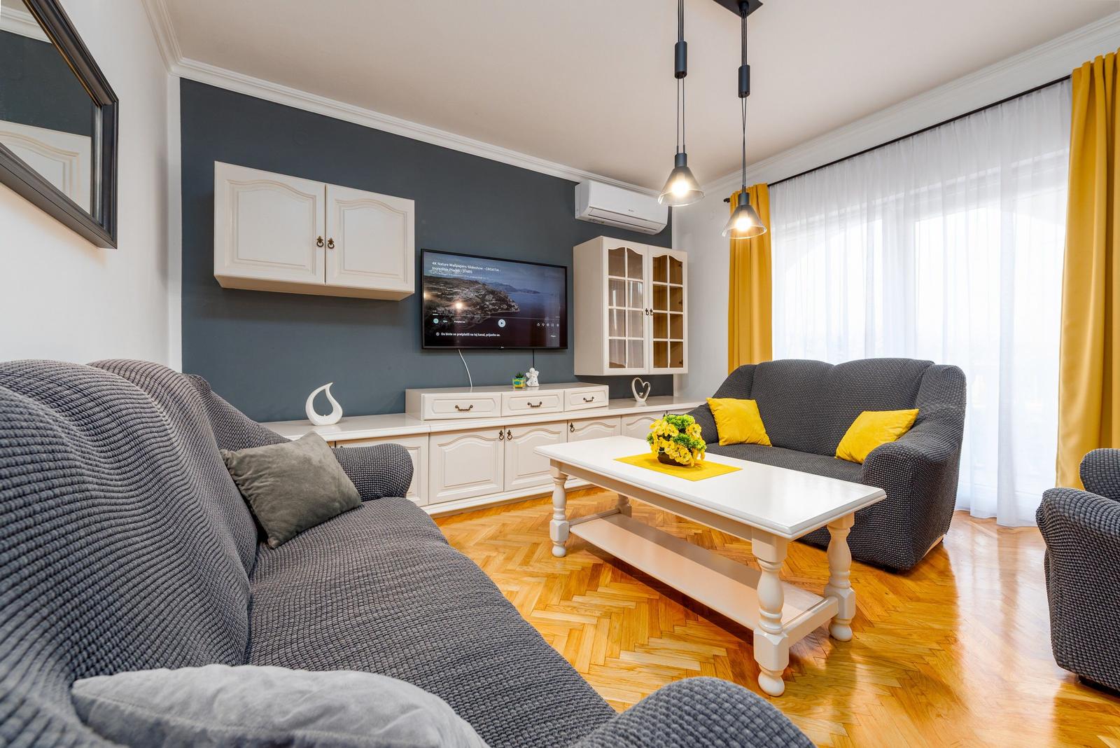 Wohnzimmer mit grauem Sofa, weißem Tisch und TV an grauer Wand.