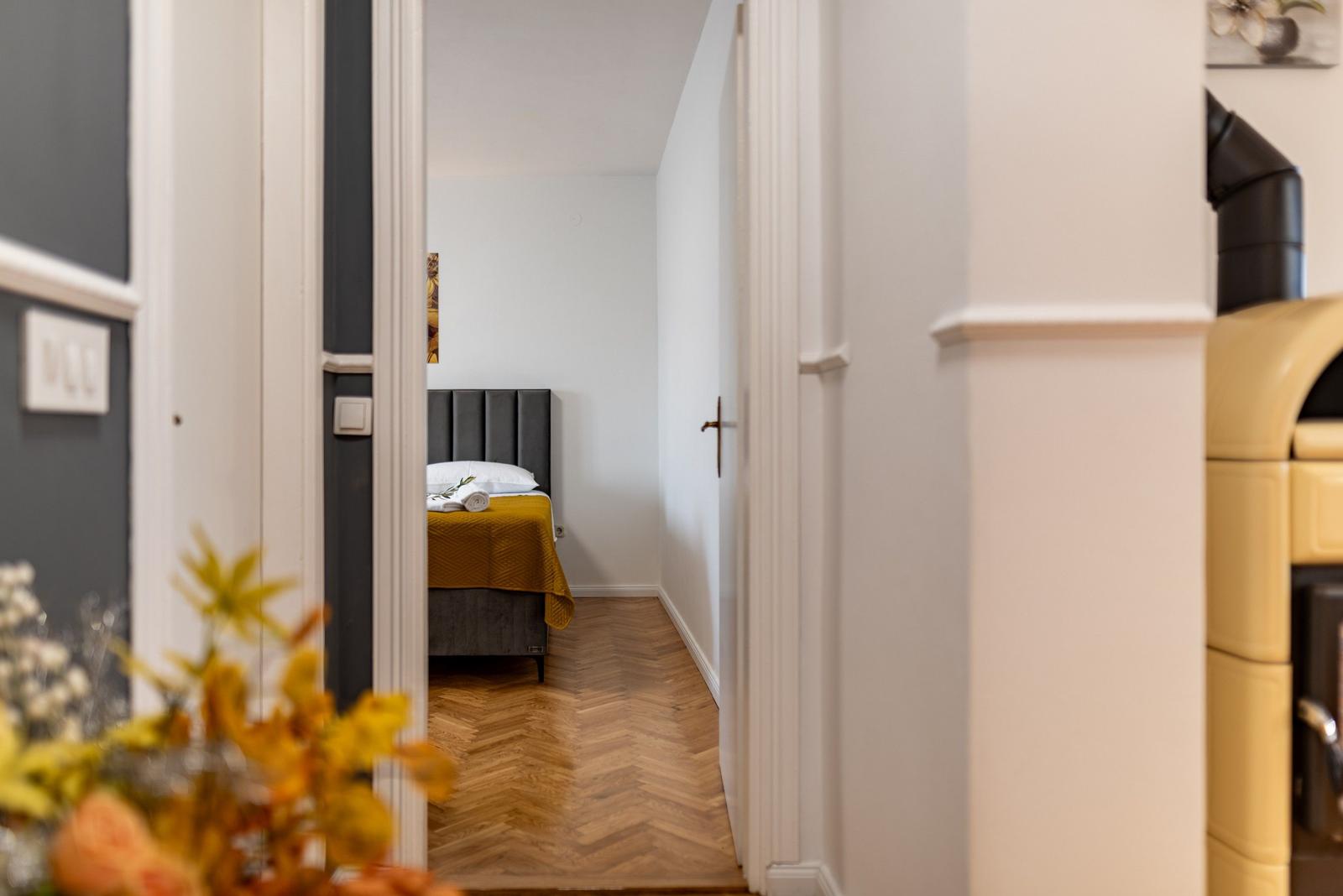 Schlafzimmer mit Bett, gelber Decke und Holzboden. Blick durch Türöffnung.