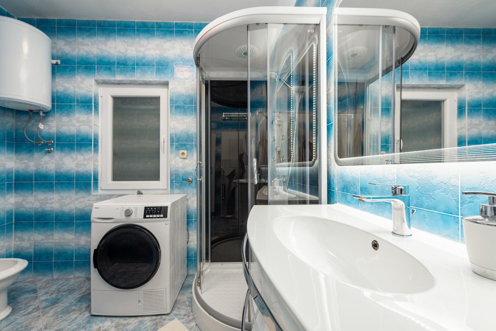 Badezimmer mit Dusche, Waschmaschine und Waschtisch