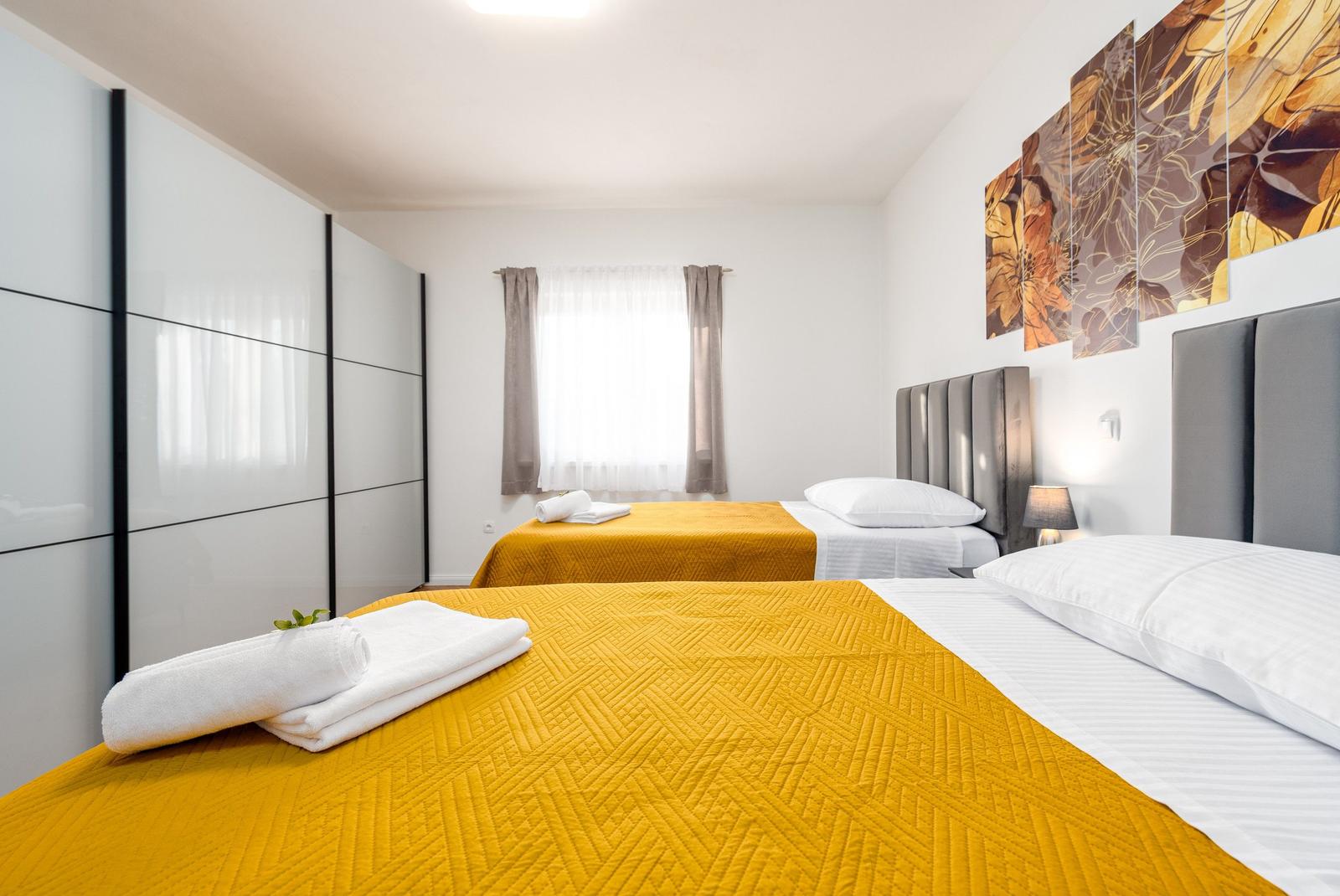 Zwei Betten mit gelben Bezügen und weißen Kissen. Wandbild und Schrank sind sichtbar.