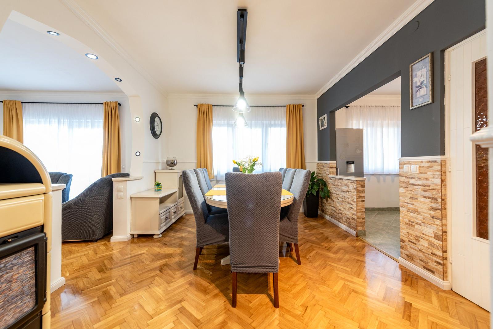 Esszimmer mit Esstisch, Stühlen und Holzboden. Durchgang zu Küche mit Steinwand.