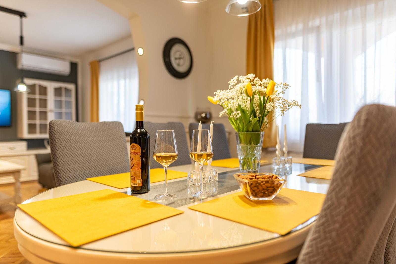 Runde Tisch mit gelben Tischsets, Wein und Blumenarrangement.