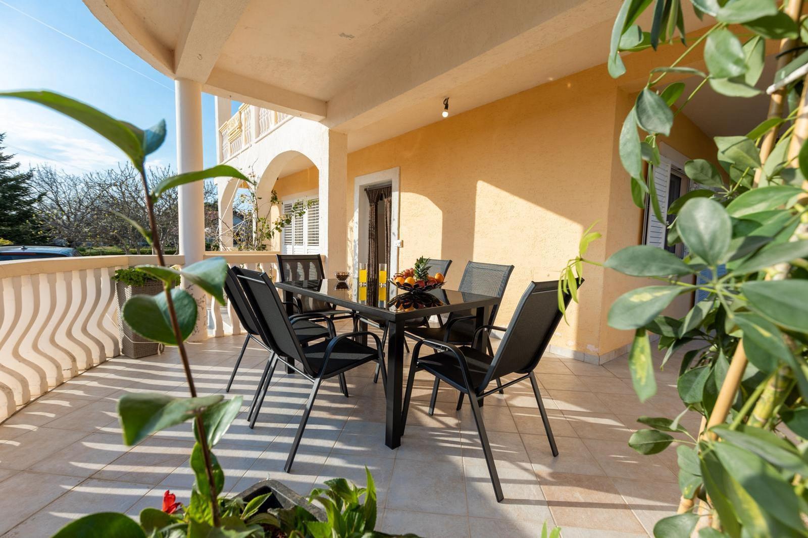 Terrasse mit Tisch und Stühlen, Pflanzen und Blick auf Hauswand.