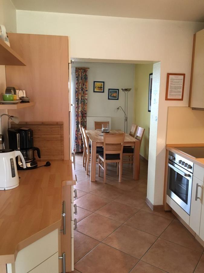 Küche mit Essbereich. Holztisch, Stühle, Kühlschrank, Herd und Kaffeemaschine.