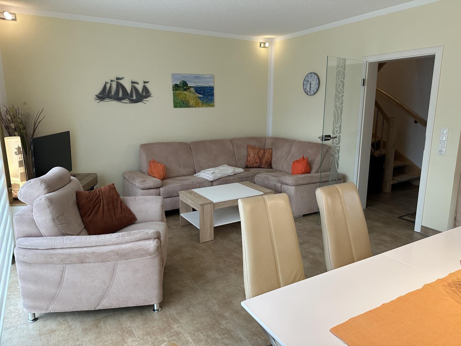 Wohn- und Essbereich mit Sofa, Sessel und Tisch. Wanddekoration und Treppe sichtbar.