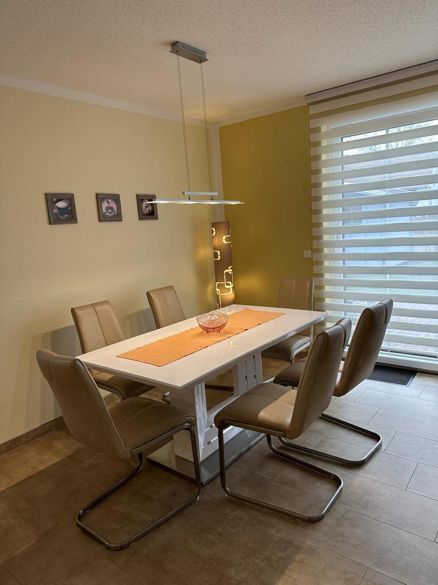 Essbereich mit weißem Tisch, sechs braunen Stühlen und Fenster mit Jalousien.