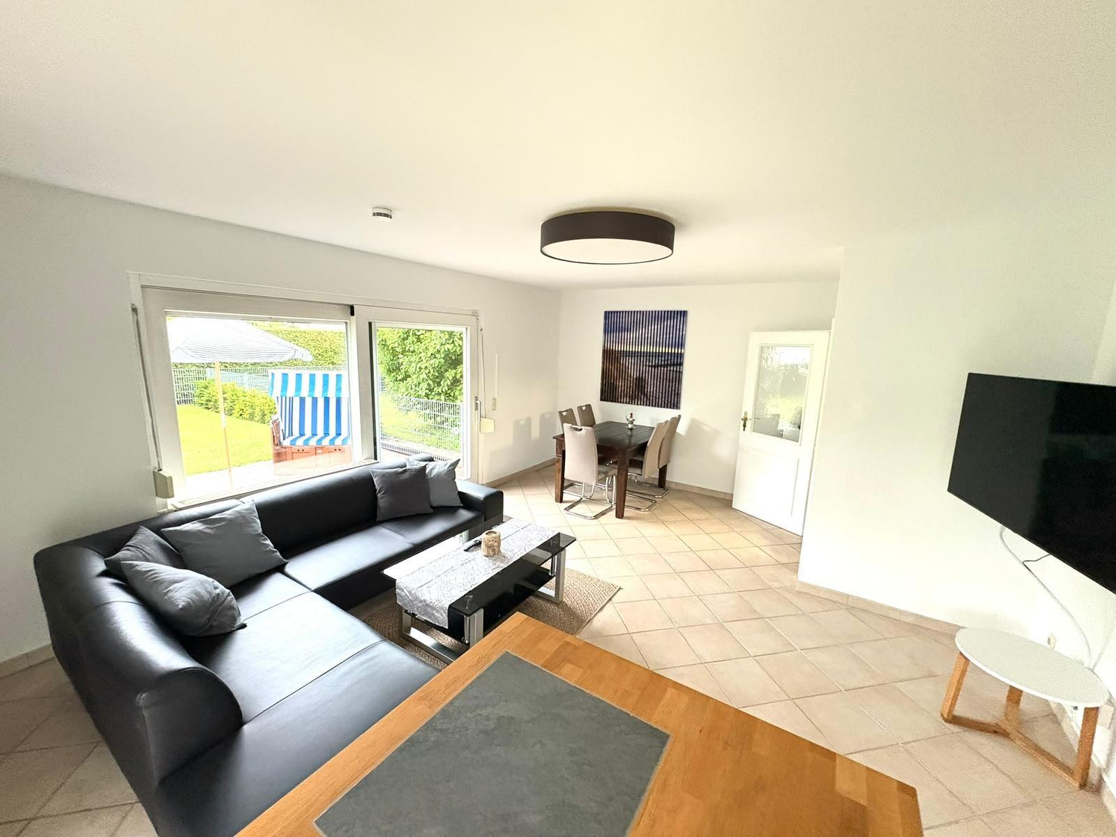 Wohnzimmer mit Sofa, Esstisch und TV. Durchgang zur Terrasse mit Strandkorb.