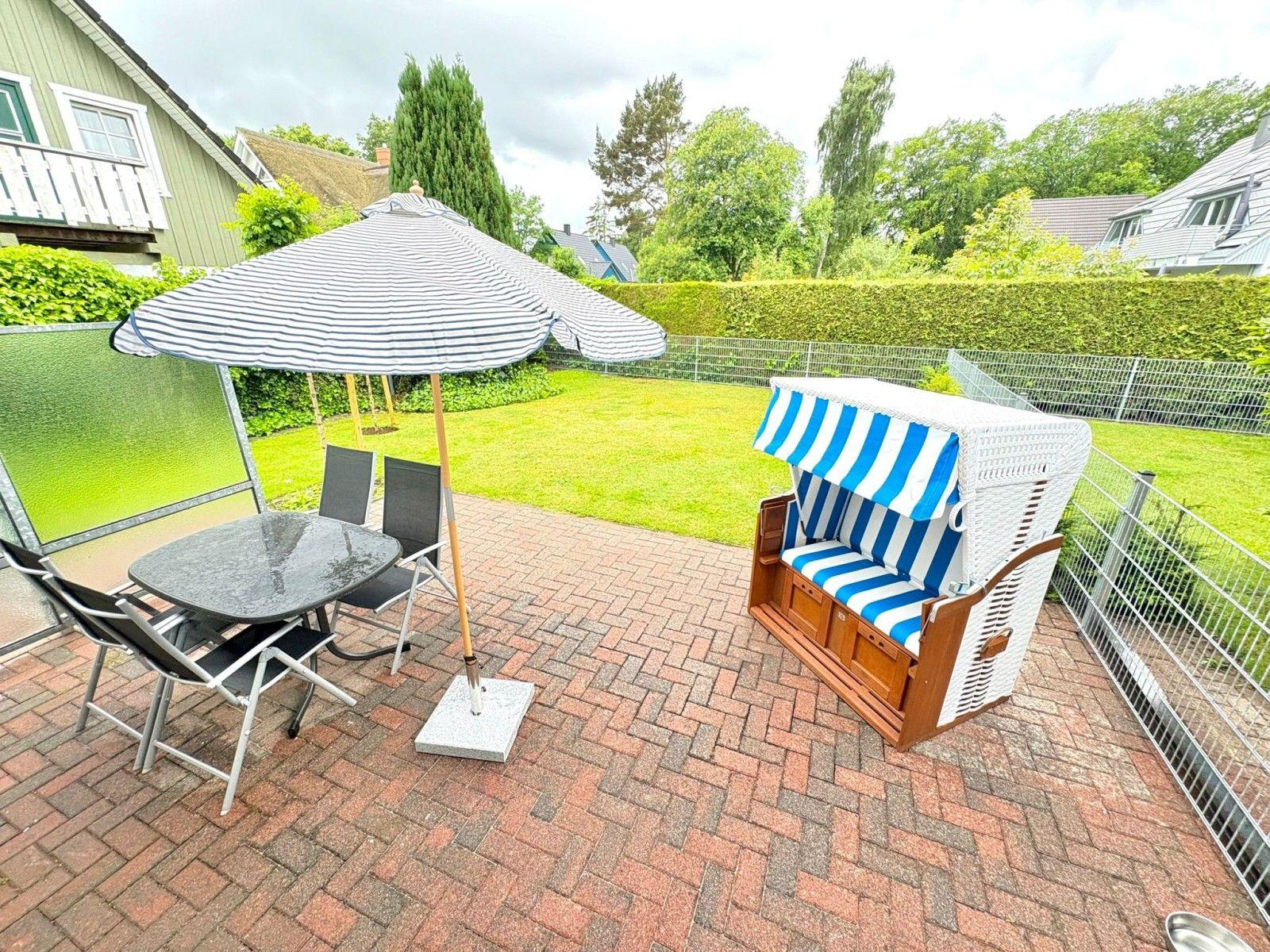 Terrasse mit Tisch, Stühlen, Sonnenschirm und Strandkorb.