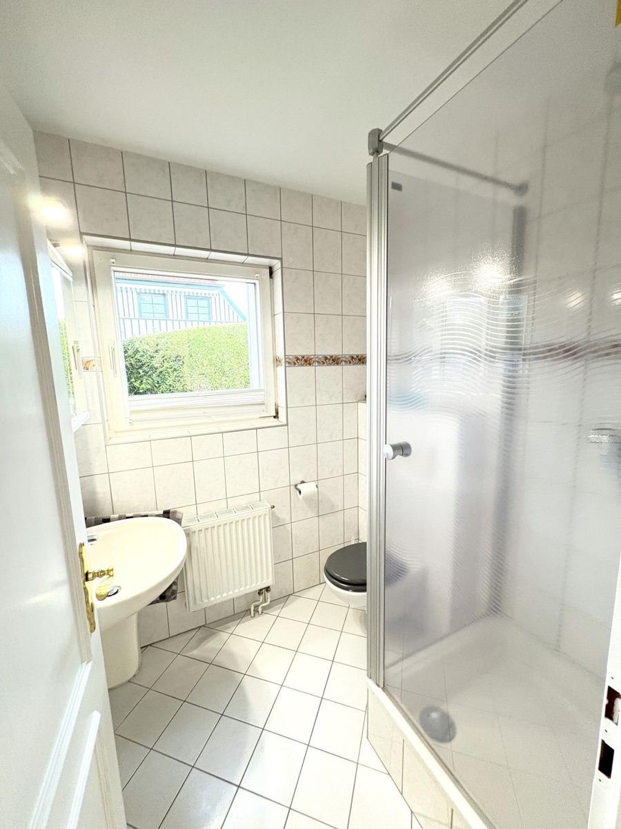 Badezimmer mit Dusche, Toilette und Waschbecken. Fenster mit Blick auf Grün.