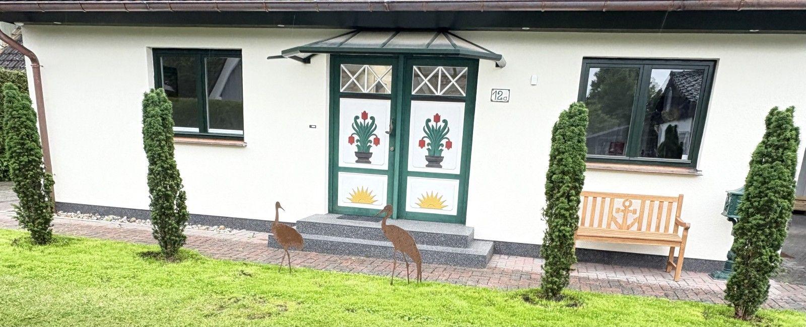 Haus mit grüner Tür, zwei Fenstern und Gartenbank mit Ankermotiv.