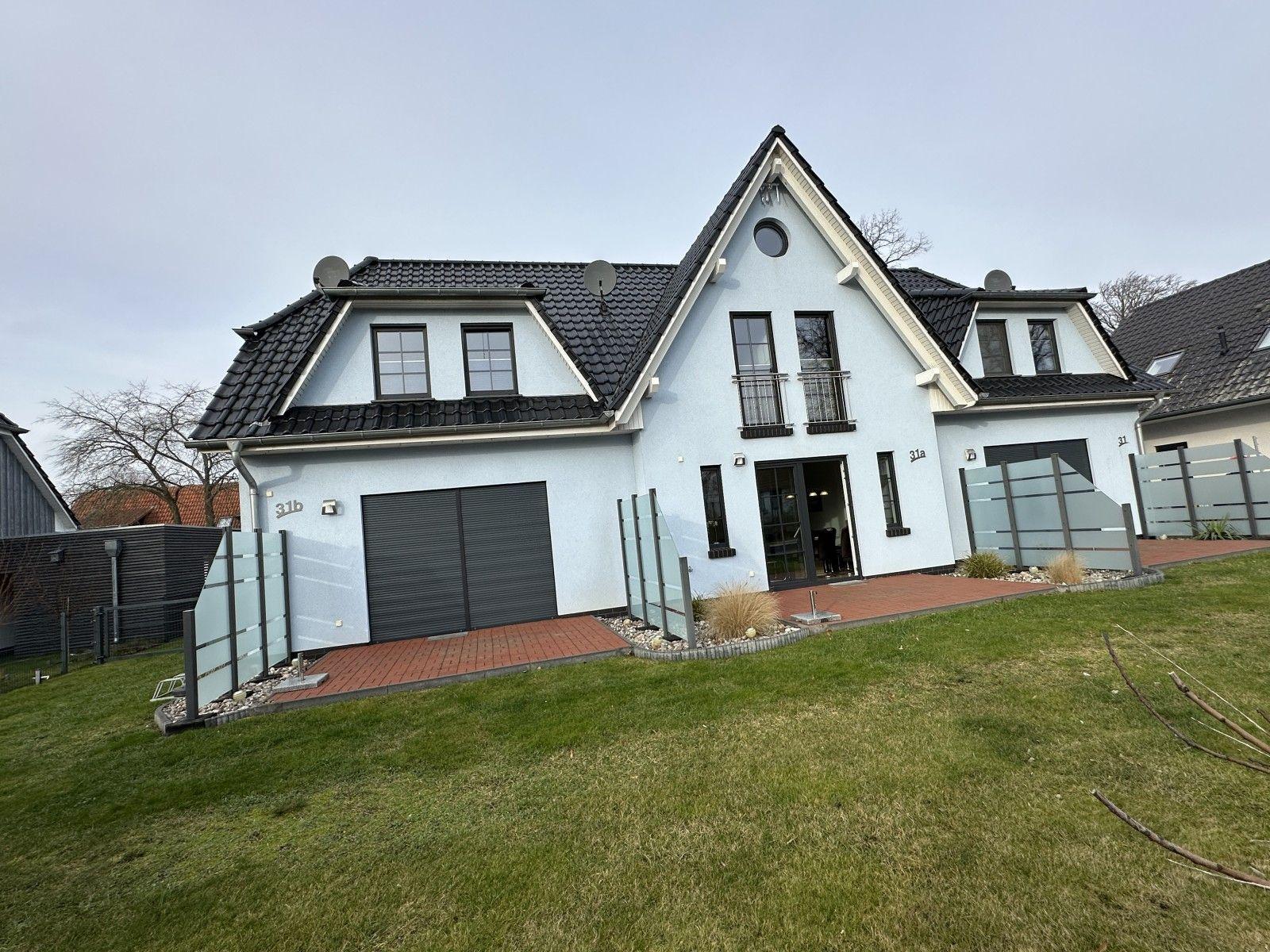 Moderne Villa mit Garage, Terrasse und Garten. Schwarze Fenster und Dachziegel.