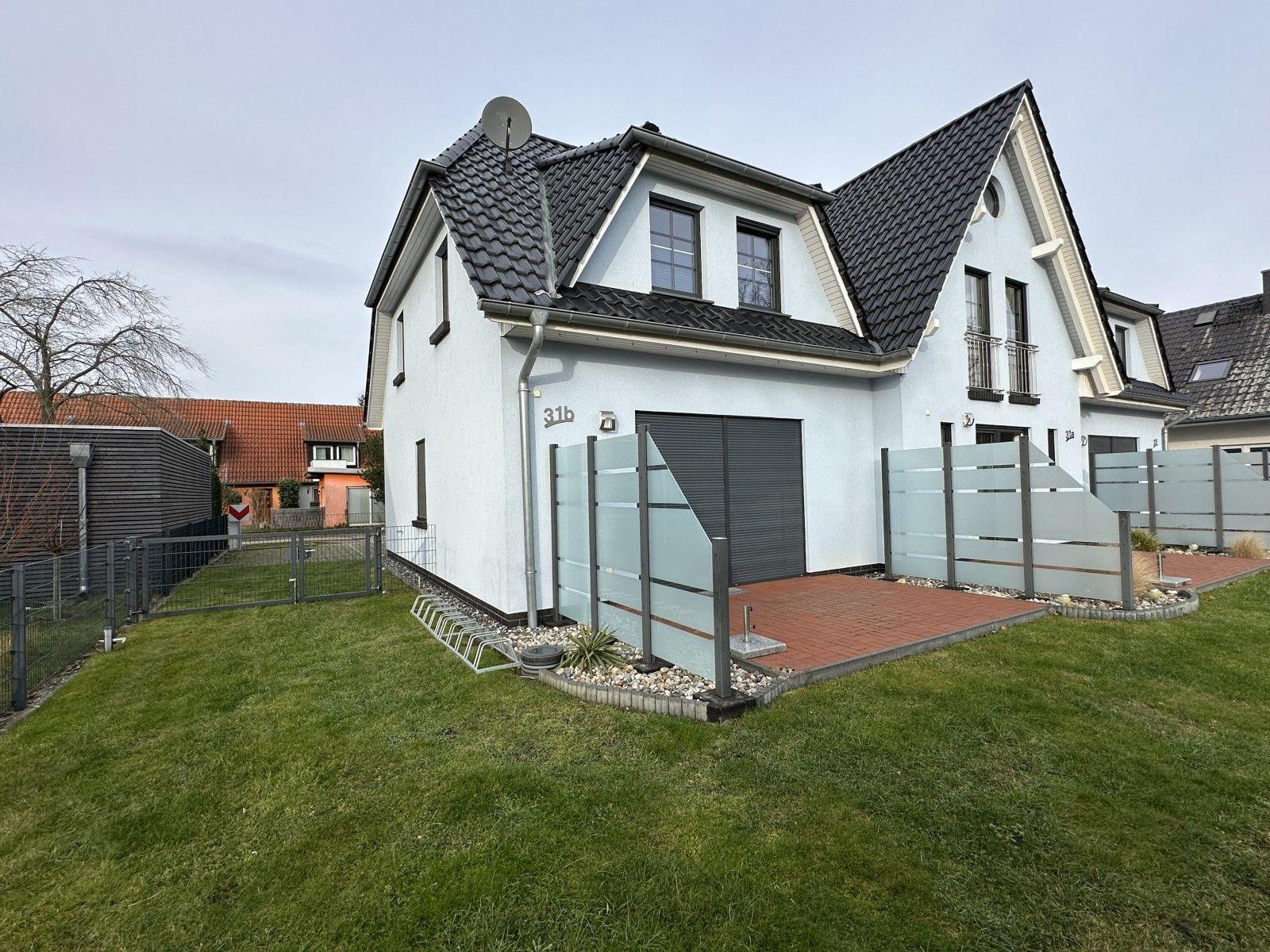 Moderne Villa mit Garage und Garten. Glasgeländer und roter Kiesweg.