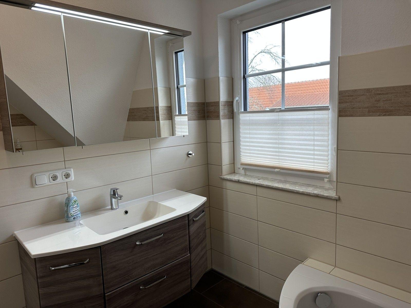 Bad mit Waschbecken, Spiegelschrank und Fenster mit Jalousie.